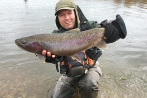 A smiling angler holds up his rainbow trout that he caught during an Alaskan fishing trip.