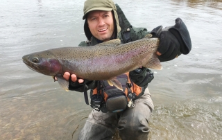 A smiling angler holds up his rainbow trout that he caught during an Alaskan fishing trip.