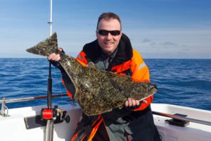An avid angler poses with a medium-sized halibut while sport fishing in Alaska.