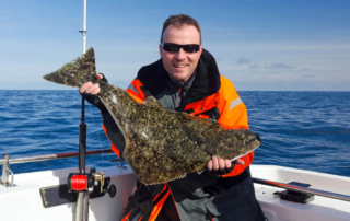 An avid angler poses with a medium-sized halibut while sport fishing in Alaska.