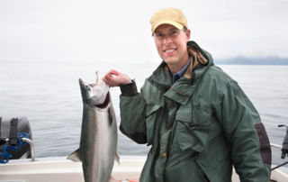 An avid angler smiles while holding a prized salmon during an Alaska fishing vacation on Angoon Island.