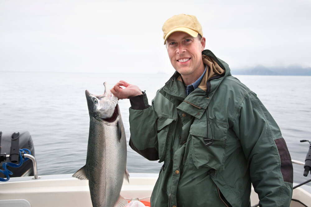 An avid angler smiles while holding a prized salmon during an Alaska fishing vacation on Angoon Island.