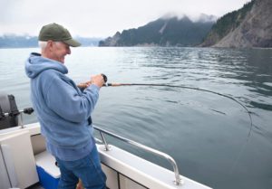 A seasoned angler enjoys his all-inclusive Alaska vacation as reels in a large salmon.
