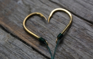 Two fish hooks symmetrically placed in the shape of a heart, representing a romantic getaway in Alaska.