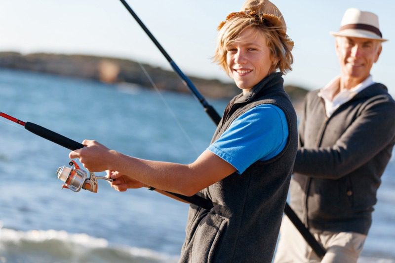 Family Fishing Trips: A young teenage boy fishing with his grandfather in Alaska.